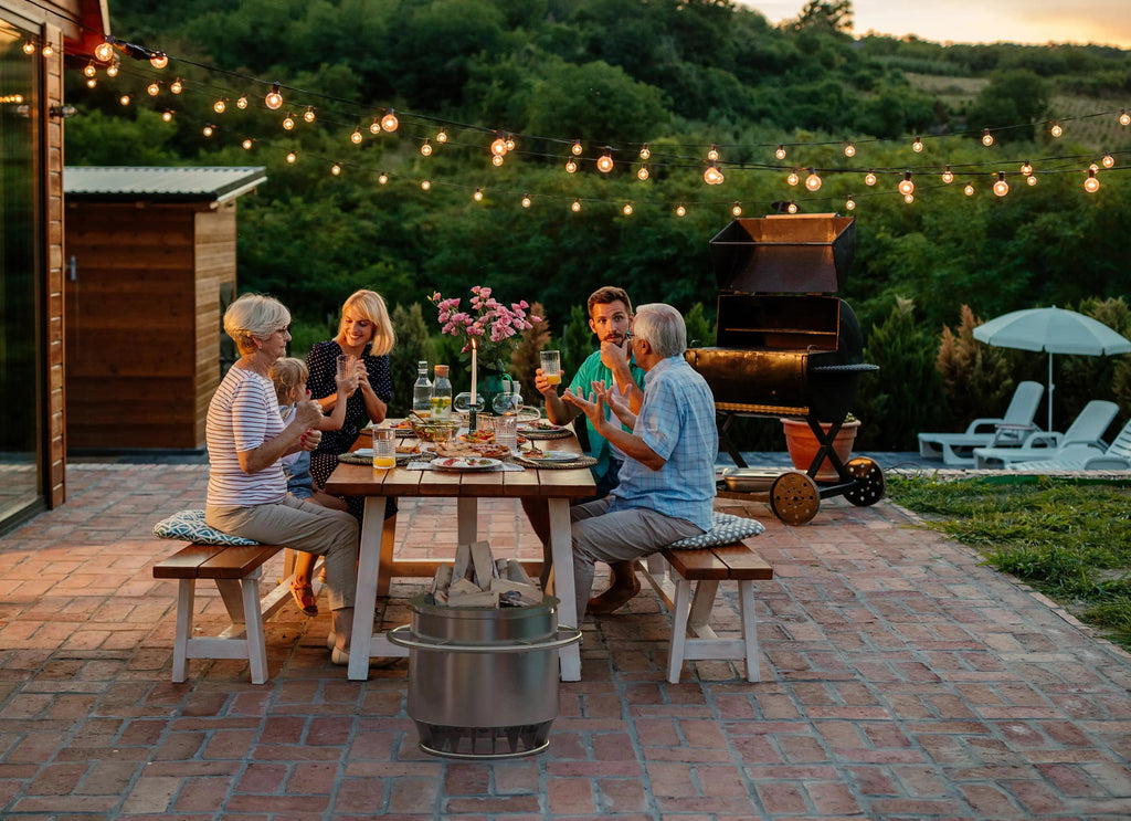 Eine Familie bei einem gemütlichen Abendessen im Garten. Der Titanstove, nichtangezündet steht vor dem Holztisch auf dem Steinboden.