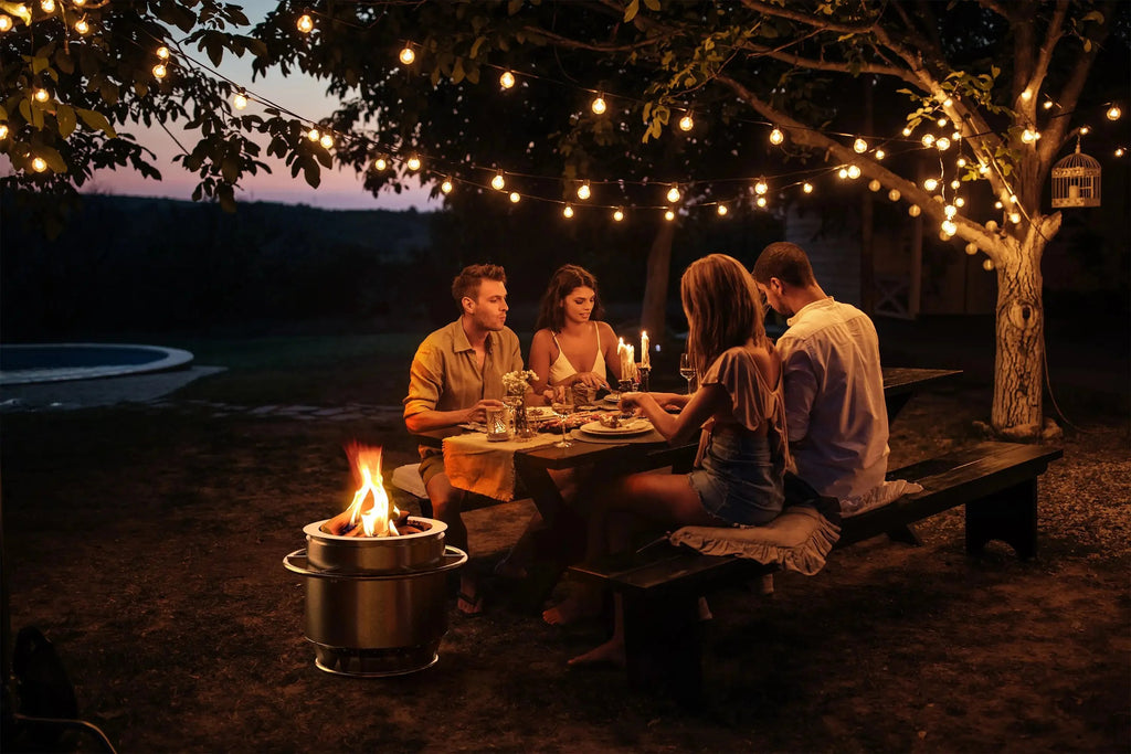 Junge Menschen die abends im Park einen entspannten Grillabend feiern und Essen. Links neben dem Tisch steht die rauchfreie Feuerschale Titanstove.